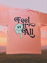 Load image into Gallery viewer, Drippy smiley face screenprinted on a salmon shirt with text that says Feel It All
