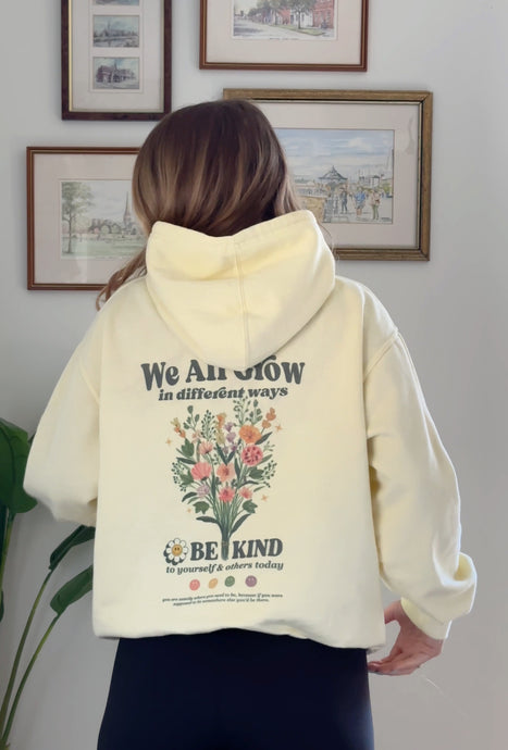 Light yellow Be Kind hooded sweatshirt with a floral design that includes embroidery and screenprinting elements